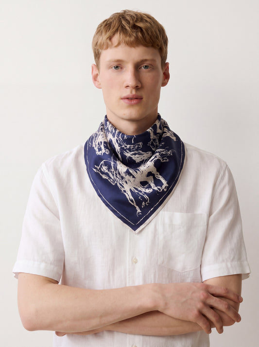 Man wearing a white shirt and a blue scarf with a dog pattern on a plain background