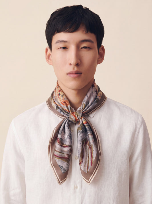 Man wearing a patterned scarf around his neck against a plain background