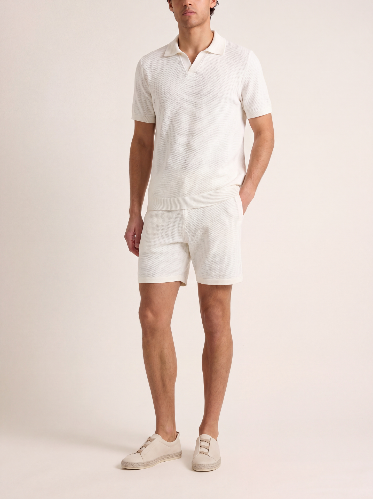 Man wearing a white polo shirt and shorts set on a plain background