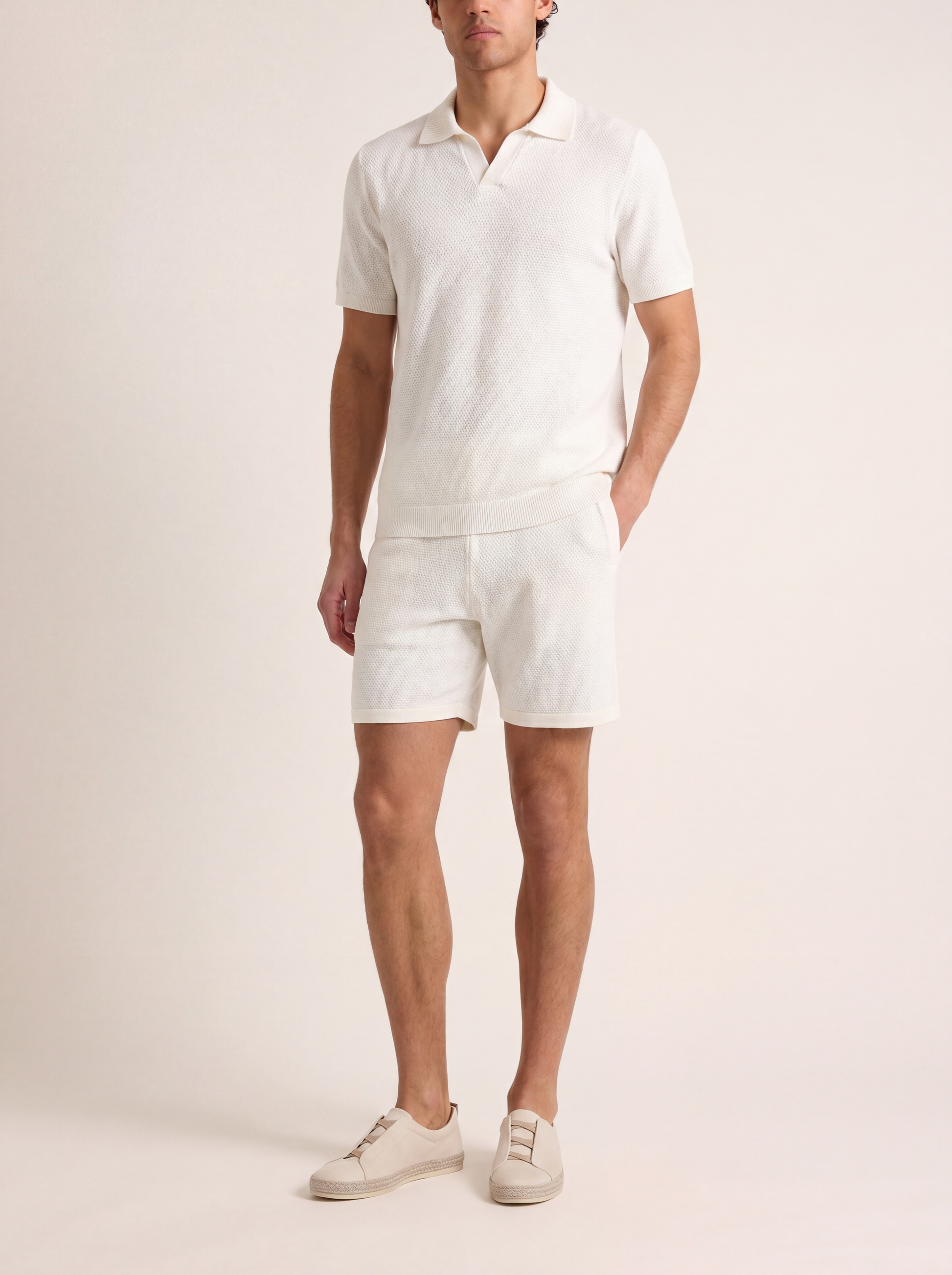 Man wearing a white polo shirt and shorts set on a plain background